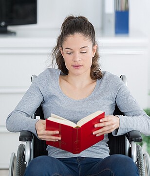 Junge Frau im Rollstuhl liest in einem Buch 