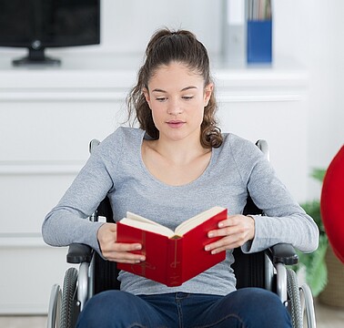 Junge Frau im Rollstuhl liest in einem Buch 