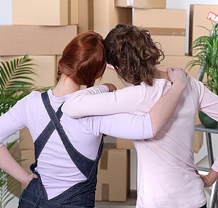 2 young women from behind arm in arm in front of moving boxes
